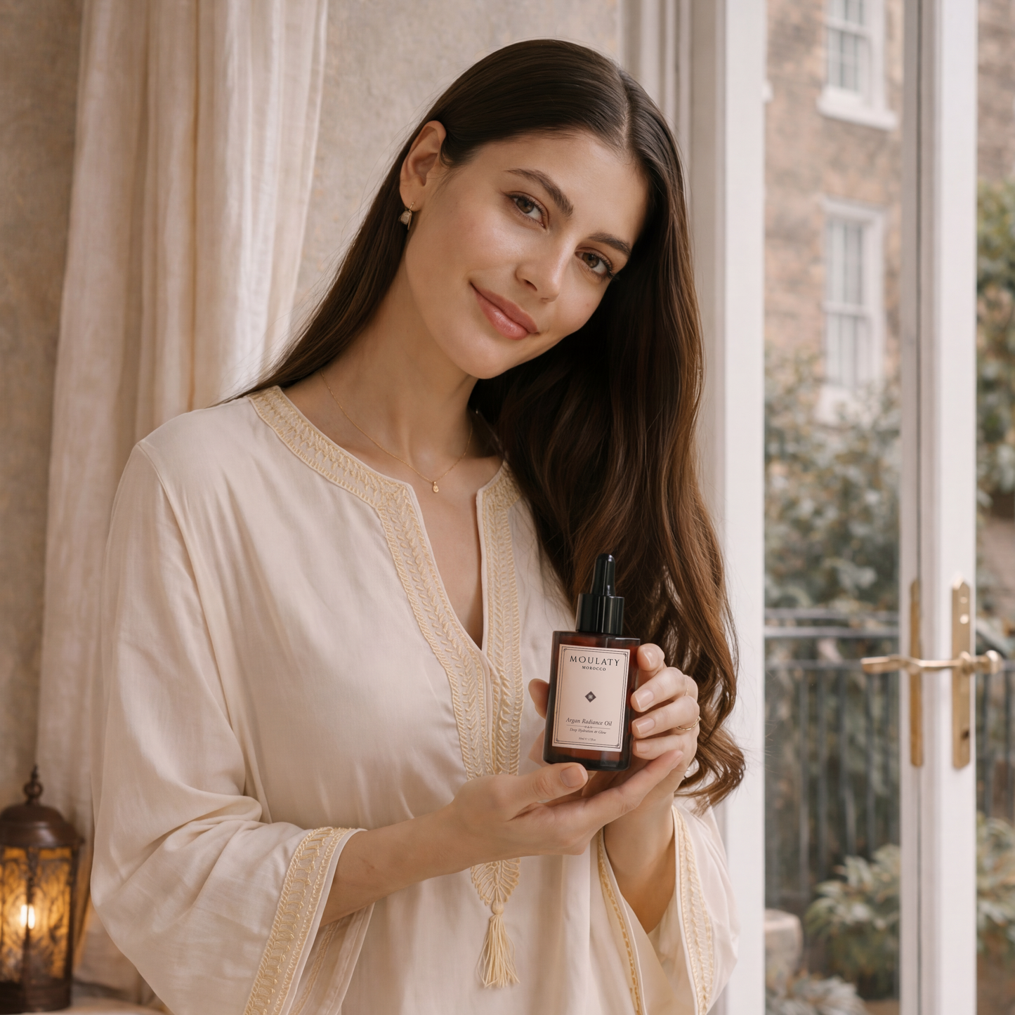 Woman in cream kaftan holding bottle of pure argan oil skincare by window, natural light