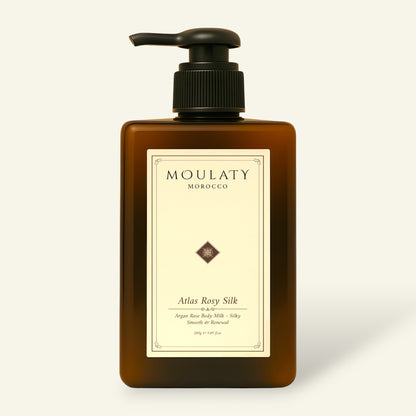 Amber pump bottle of Atlas Rosy Silk argan rose body milk against a beige background.