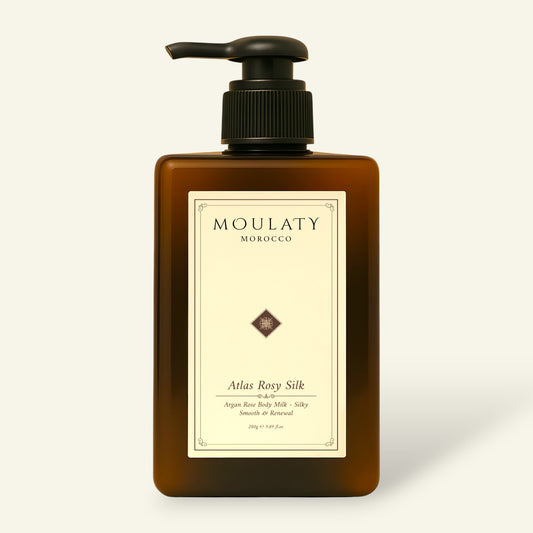 Amber pump bottle of Atlas Rosy Silk argan rose body milk against a beige background.