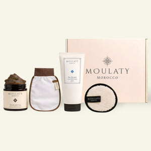 Moroccan skincare set with black soap, Blue Nila mask, exfoliating mitt, pad, and gift box.