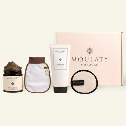 Moroccan skincare set with black soap, Blue Nila mask, exfoliating mitt, pad, and gift box.