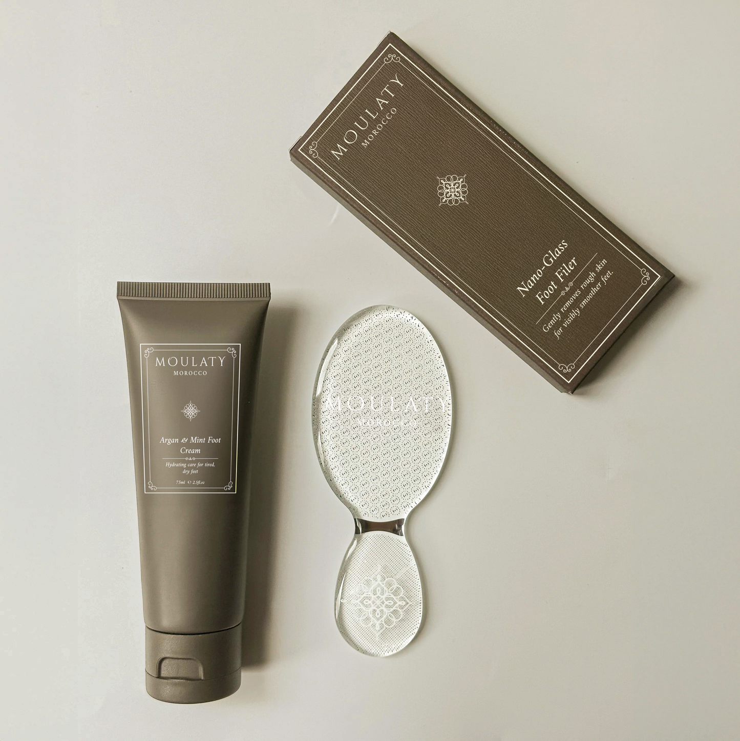 Argan and mint foot cream tube, nano glass foot file, and packaging on a neutral background.